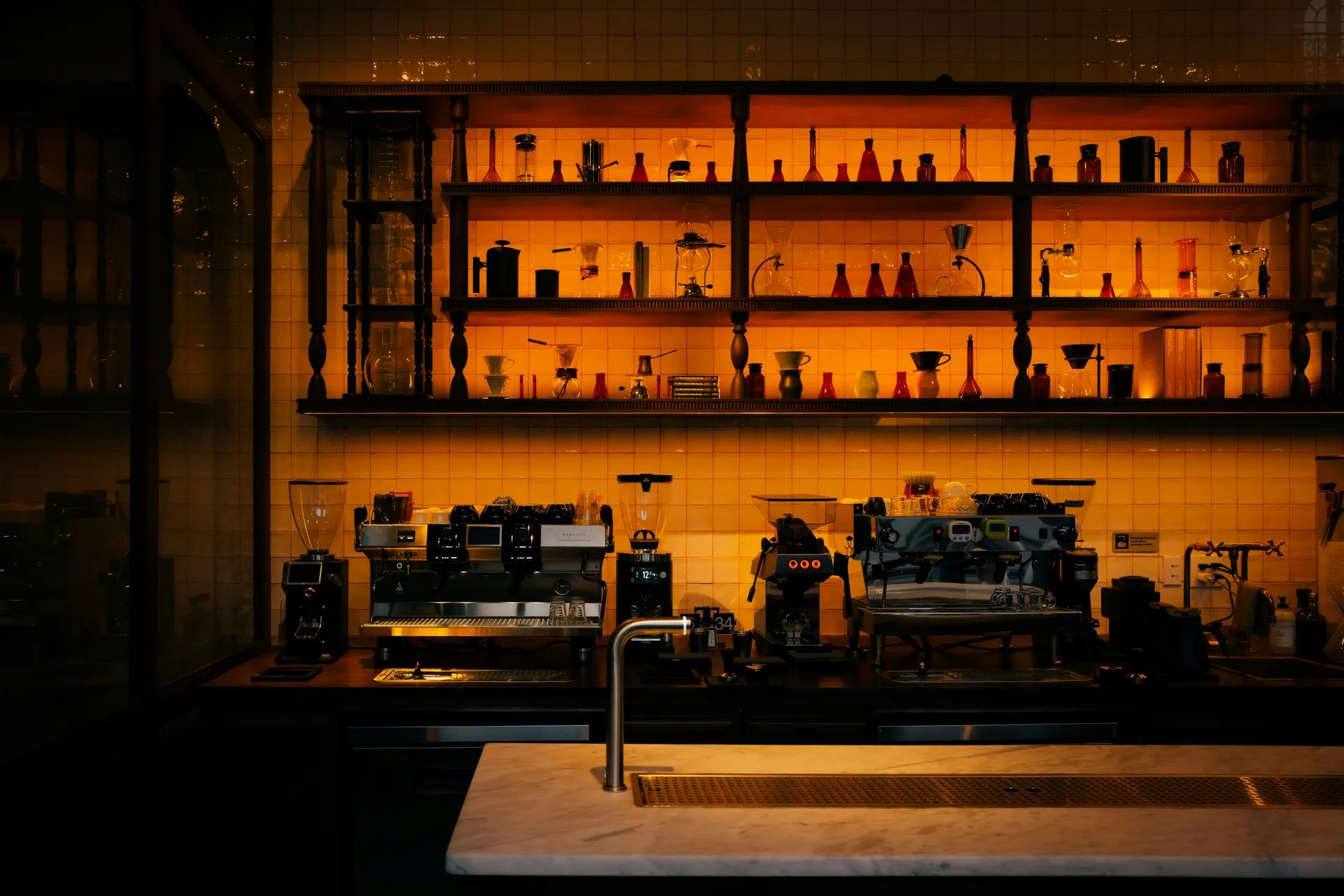 An amber-lit coffee bar with espresso machines and shelves of brewing equipment